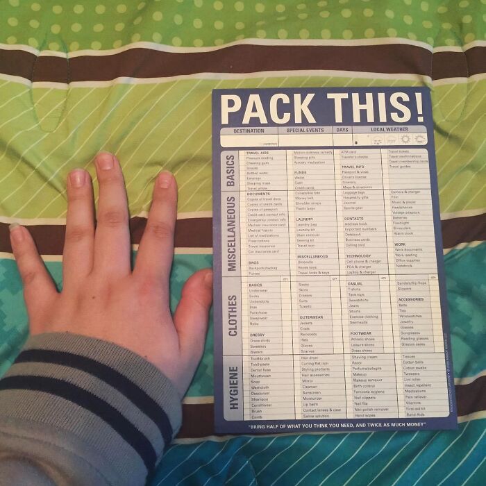 Packing list for travel on a colorful bedspread with a hand nearby.