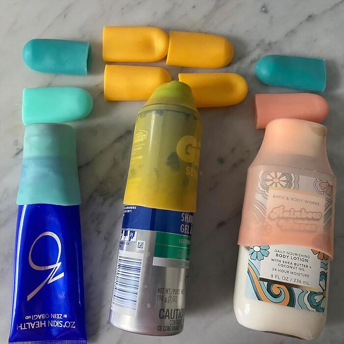 Travel items: sunscreen, shaving gel, and lotion with silicone travel covers on a marble surface.