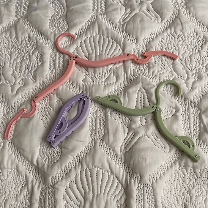 Foldable travel hangers in pink, purple, and green on a patterned white blanket.