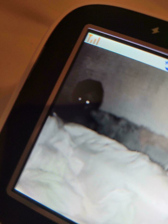 Night vision baby monitor screen showing a dark figure with glowing eyes behind a blanket, capturing a funny dad moment.