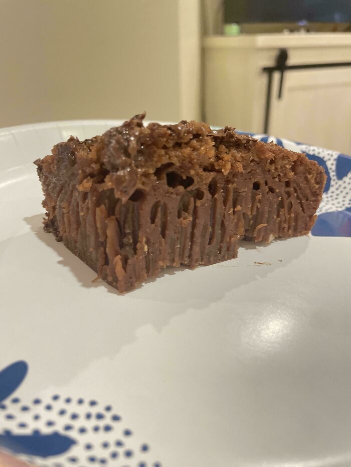 Close-up of a failed baking attempt showing a dense, c*****d chocolate dessert on a plate, a funny and awkward moment.
