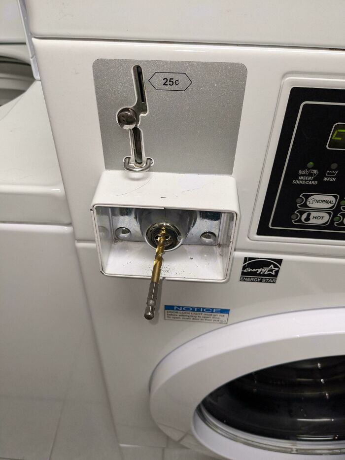 Laundry machine coin slot with a drill bit stuck inside, a funny and awkward moment when an attempt didn't go as expected.
