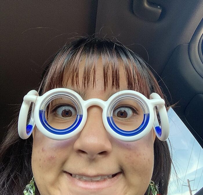 Person wearing unique round glasses with blue accents smiling joyfully, spreading joy with amazing discoveries theme.