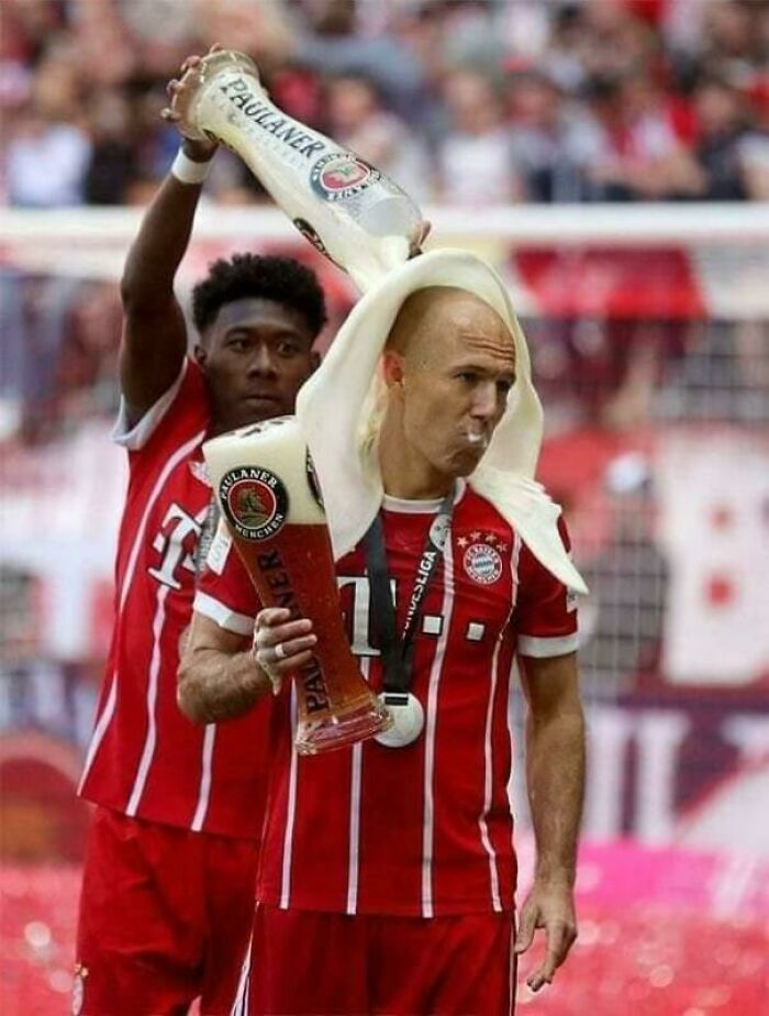 Confusing image of a soccer player being poured with beer while holding a tall glass during a celebration.
