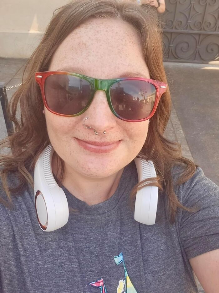 Smiling woman with colorful sunglasses and white headphones in a casual setting, capturing attention.
