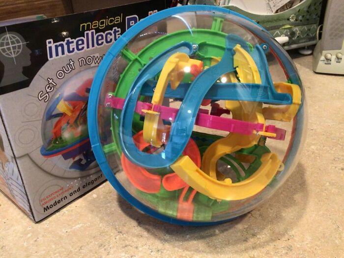 Colorful 3D maze puzzle ball toy placed on a counter next to its packaging, showcasing an amazing discovery.