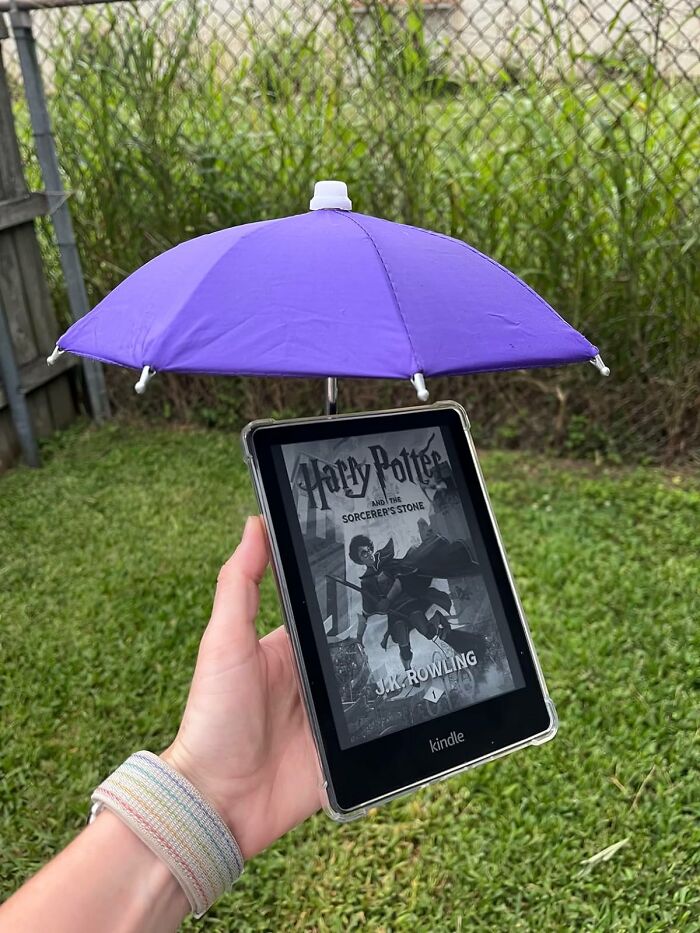 Kindle e-reader with a small purple umbrella attached, showcasing a random useful gadget outdoors with grass background.