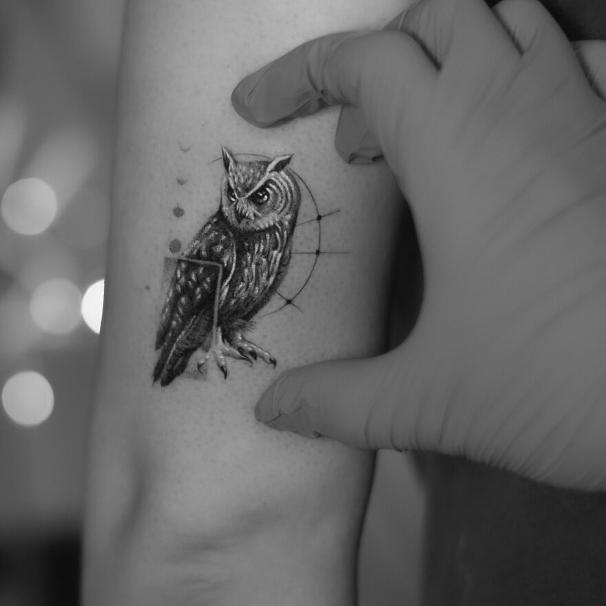 Single needle tattoo of an owl on an arm, detailed design with shading, artist wearing gloves for precision work.