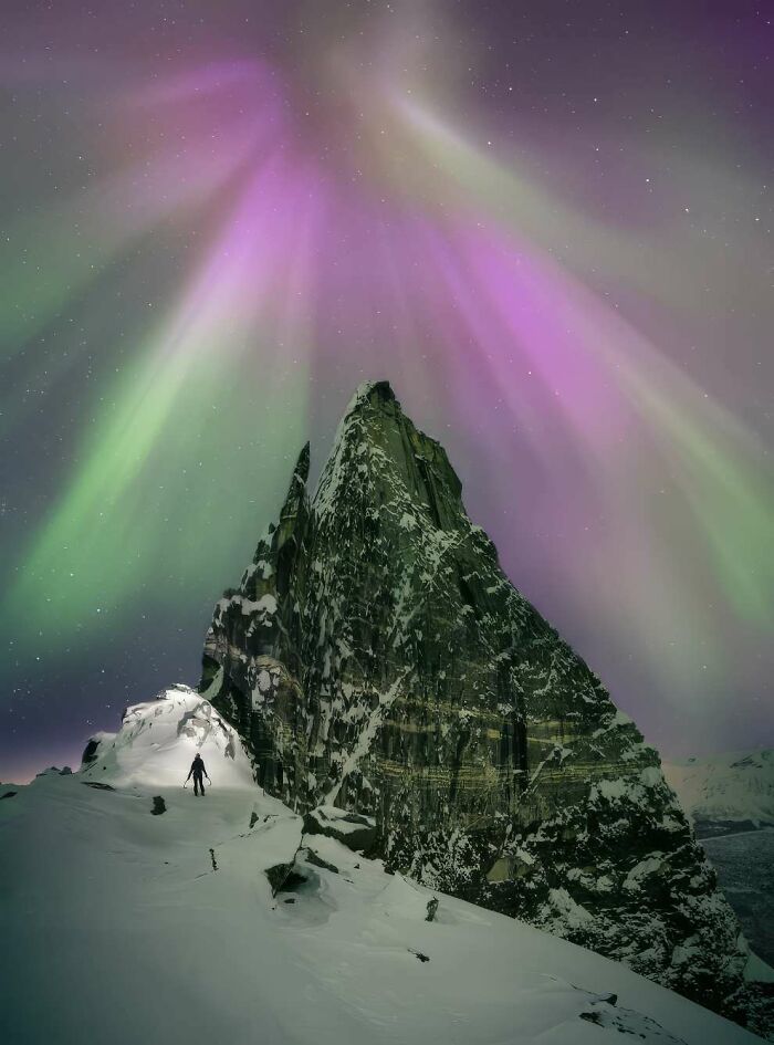 Snow-covered mountain peak under vibrant purple and green northern lights in breathtaking landscape photo from 2024 ReFocus Awards.