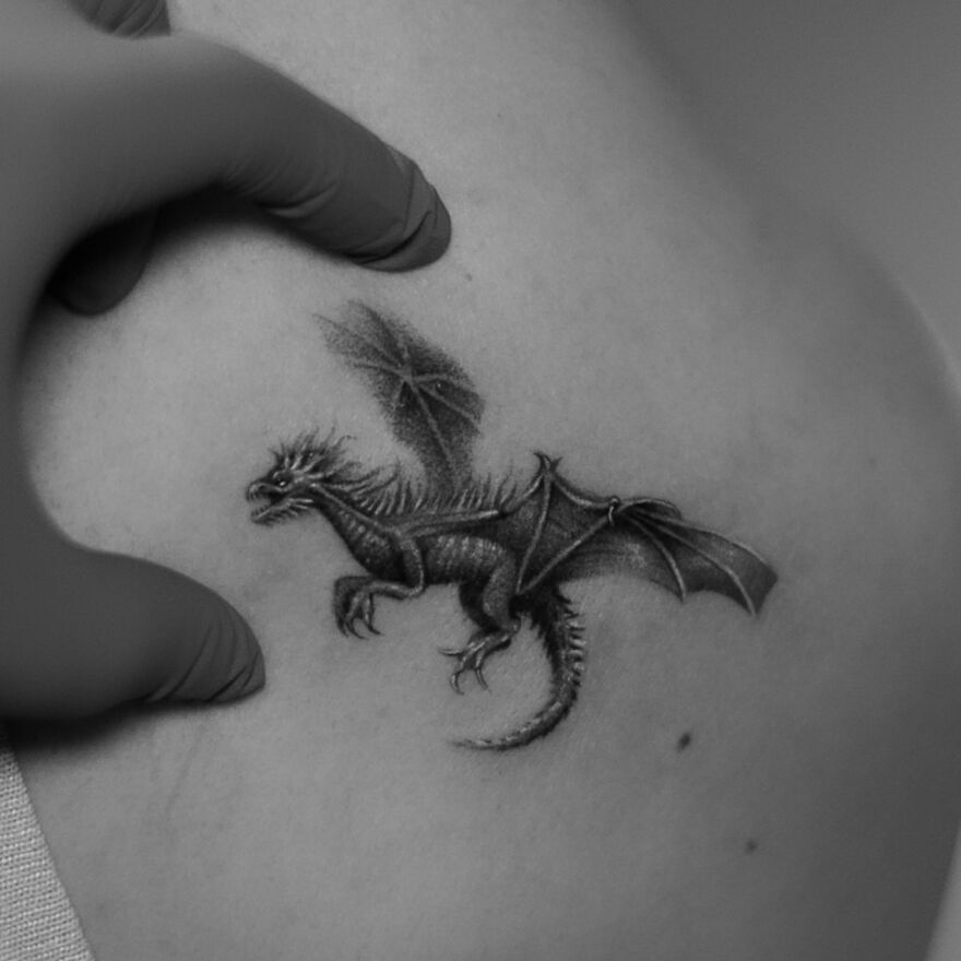 A detailed dragon tattoo created with a single needle on a person's back, surrounded by a gloved hand.