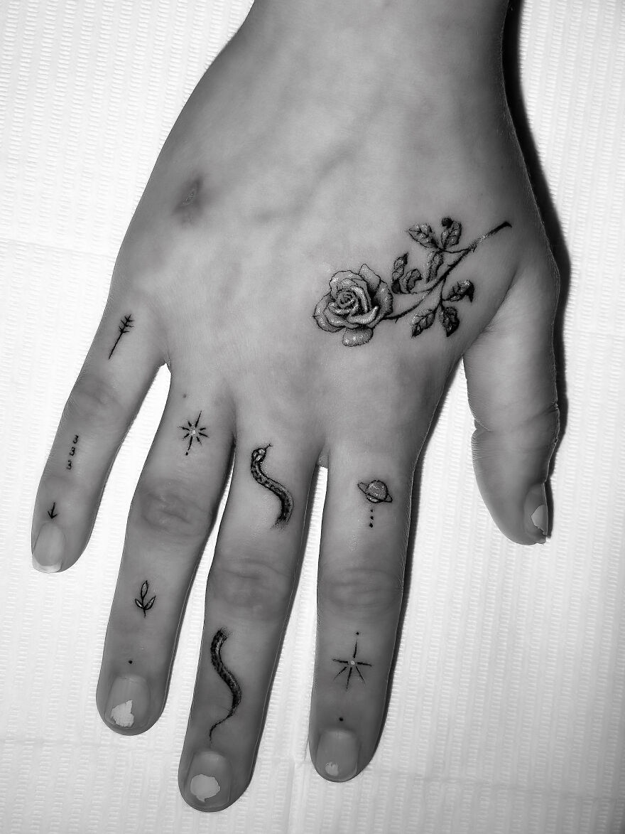 Hand with single needle tattoos, featuring a rose and various small designs.