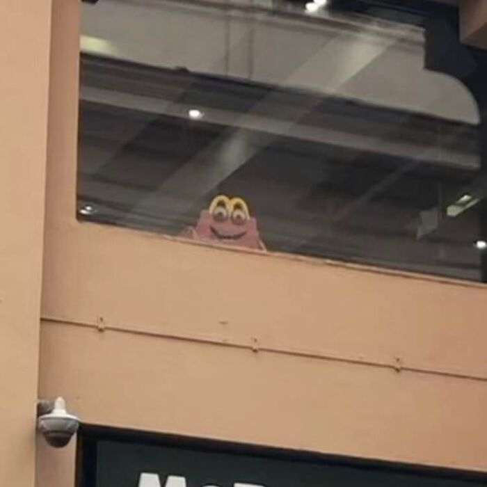 A cursed meme featuring a strange character peeking from behind a window in an urban building setting.