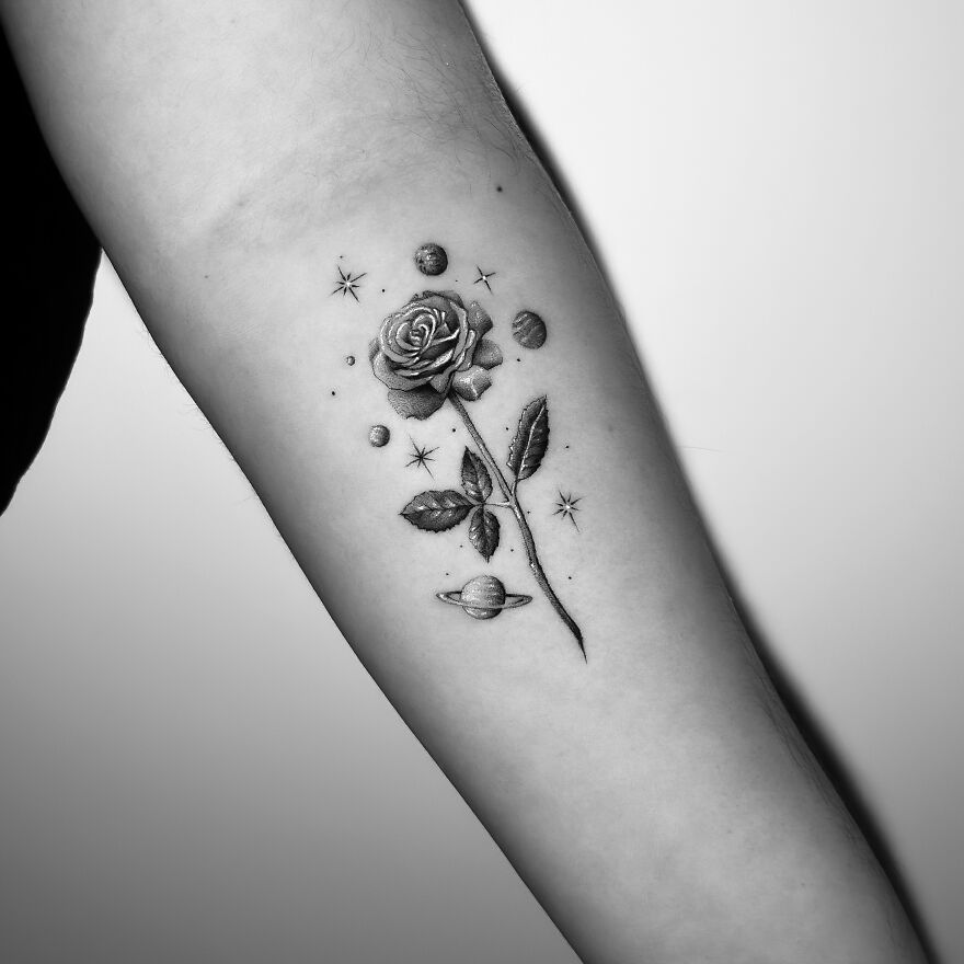 Single needle tattoo of a rose with planets and stars on an arm.