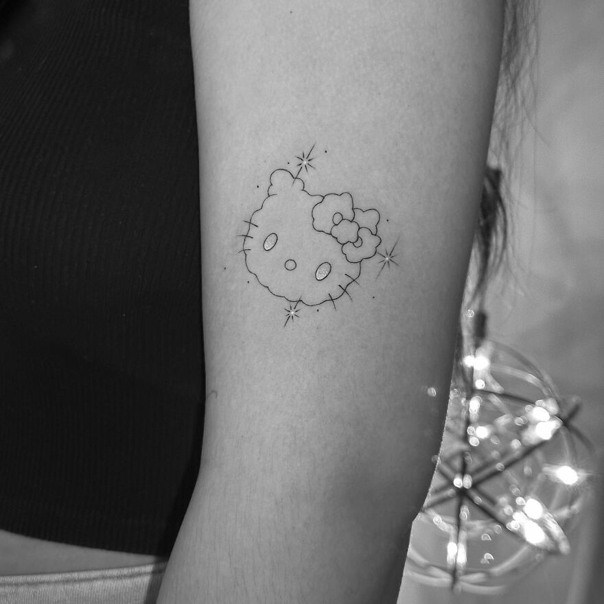 Single needle tattoo of a cute character on forearm, with sparkles, in black and gray style.