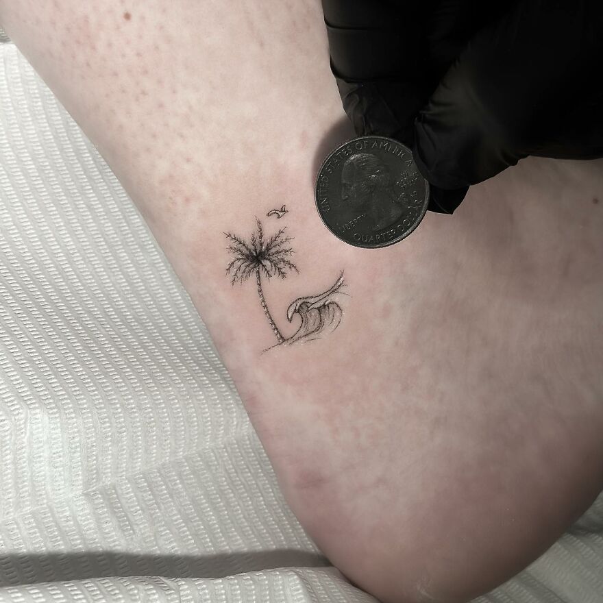 Single needle tattoo of a palm tree and wave on an ankle, shown next to a quarter for size comparison.