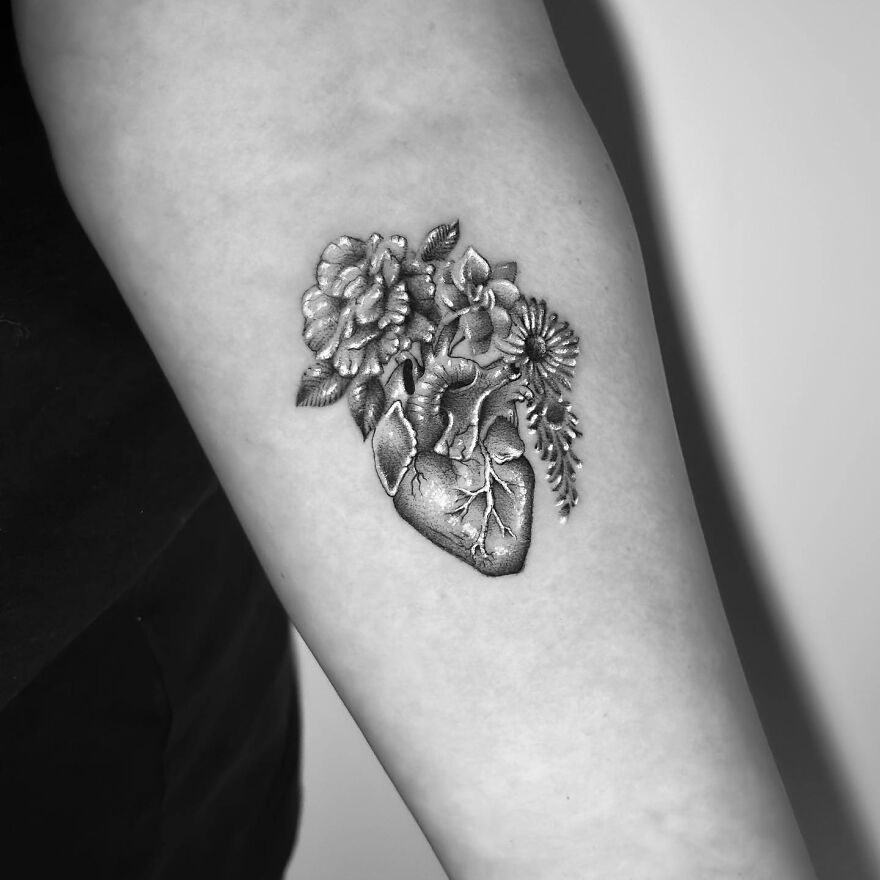 Single needle tattoo of a heart intertwined with flowers on forearm.