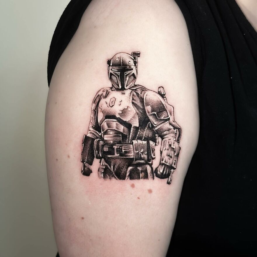 Single needle tattoo of a Mandalorian character on the upper arm, showcasing detailed shading and line work.