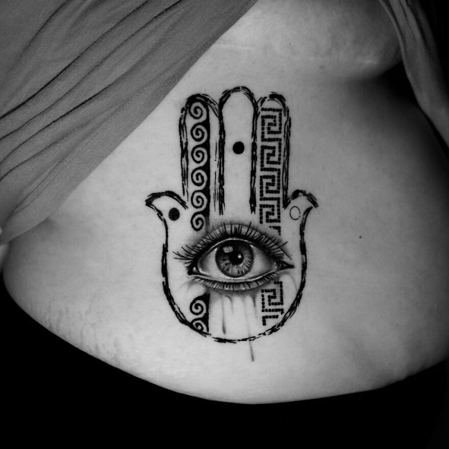 Single needle tattoo of a Hamsa hand with an eye on skin, featuring intricate patterns in black and white.