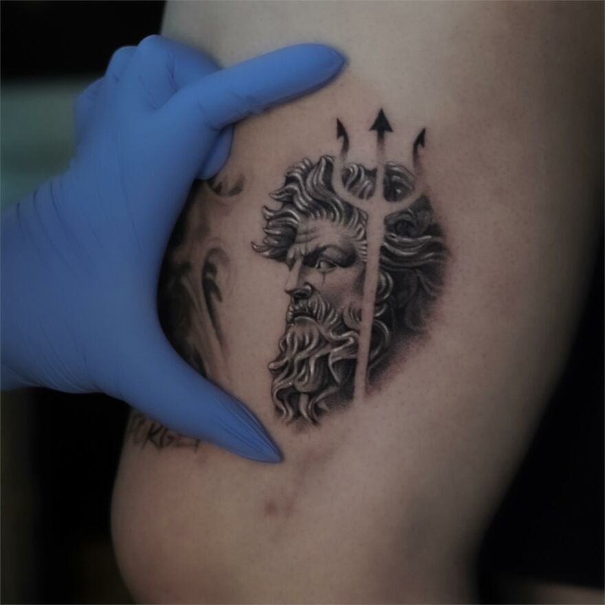 Single needle tattoo of a bearded man with a trident, held by a gloved hand.
