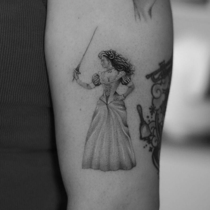 Single needle tattoo of a woman in a gown holding a sword on an arm.