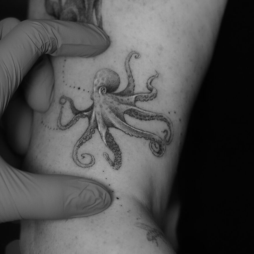 Single needle octopus tattoo design on arm, showcasing detailed line work by a tattoo artist with gloves.