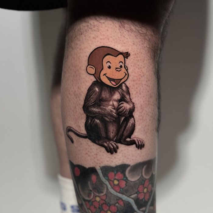A tattoo merging cartoon and realistic styles, featuring a monkey with a cartoon head and realistic body on a person's leg.