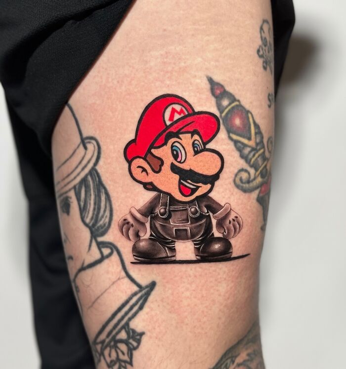 Tattoo combining two artistic styles featuring a cartoon character with vibrant red hat and black outfit on an arm.