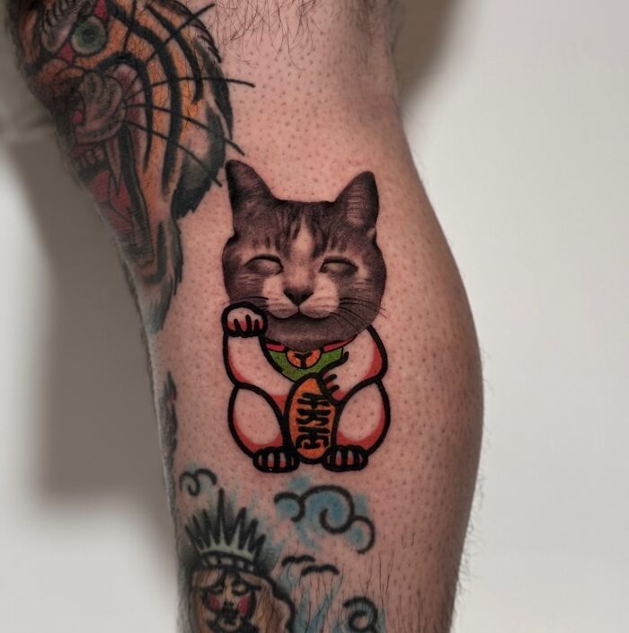 Tattoo combining traditional and photorealistic styles, depicting a cat with elements of a lucky cat design.