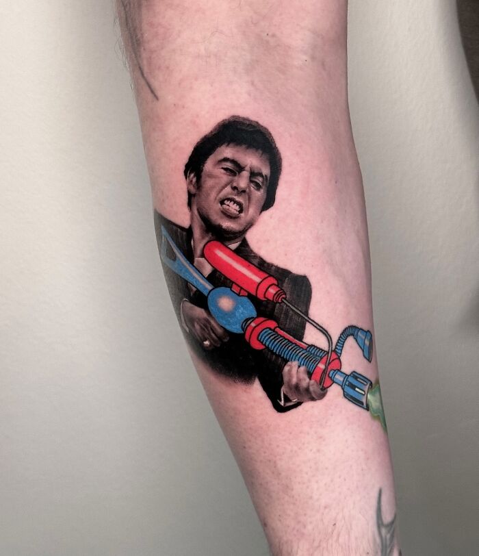 Tattoo on arm merging realism and cartoon styles, featuring a person with a colorful toy gun.
