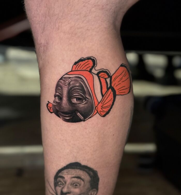 Tattoo of a clownfish with a human face seamlessly merging two artistic styles on a person's calf.