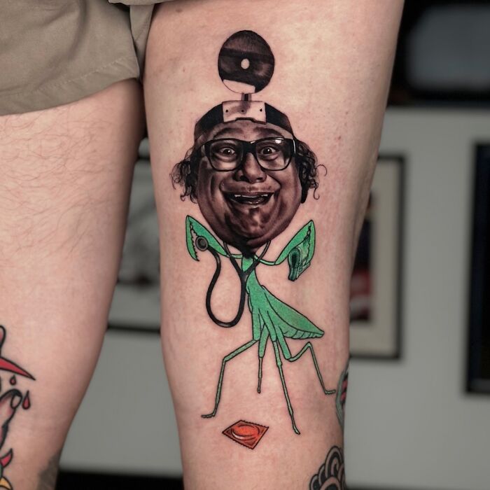 Tattoo merging two artistic styles, featuring a humorous portrait with a mantis body, on a person's thigh.
