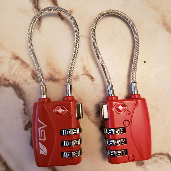 Two red TSA-approved combination locks on a marble surface, essential travel items to avoid common mistakes.
