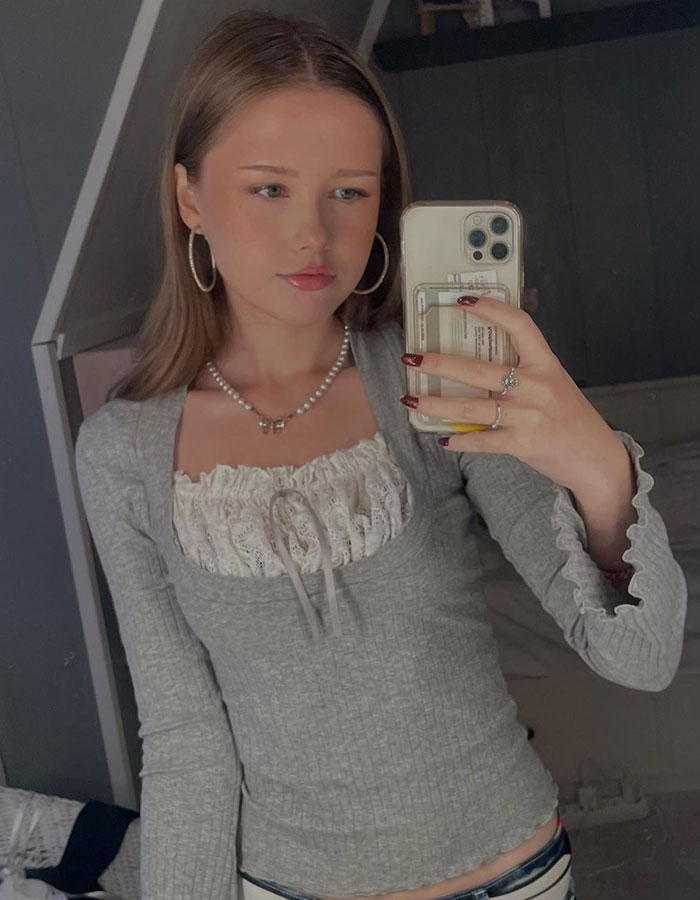 Young woman taking a selfie, appearing baffled as strangers have a picnic in her yard in the background.