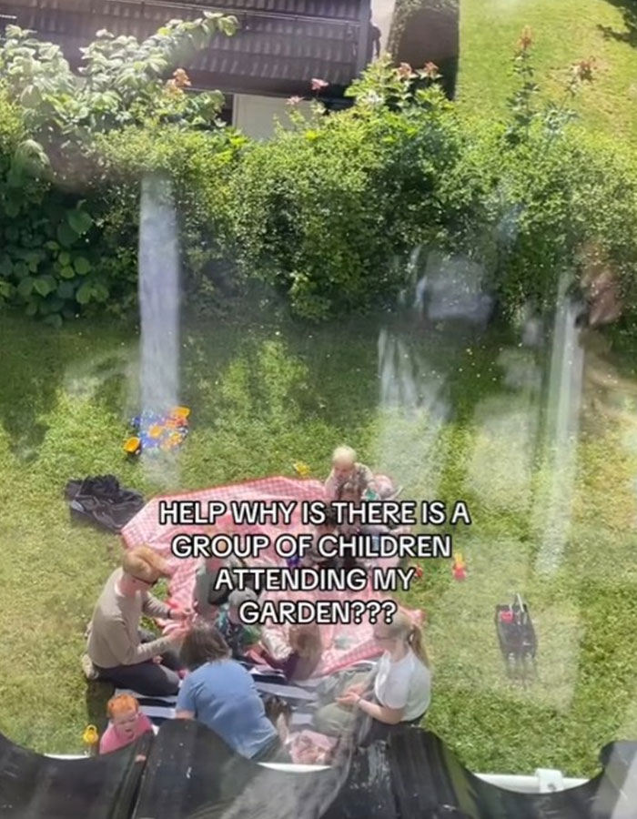 Group of strangers having a picnic in yard while woman watches, baffled and confused by the unexpected gathering.