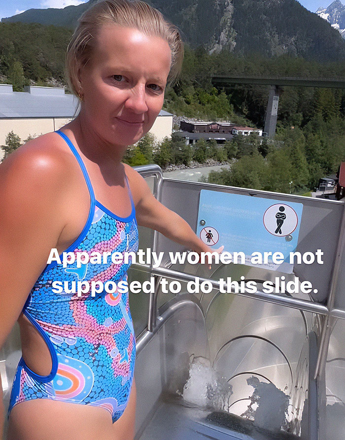 Woman in a colorful swimsuit at the top of an extreme waterslide, challenging the strict ban for women to ride.