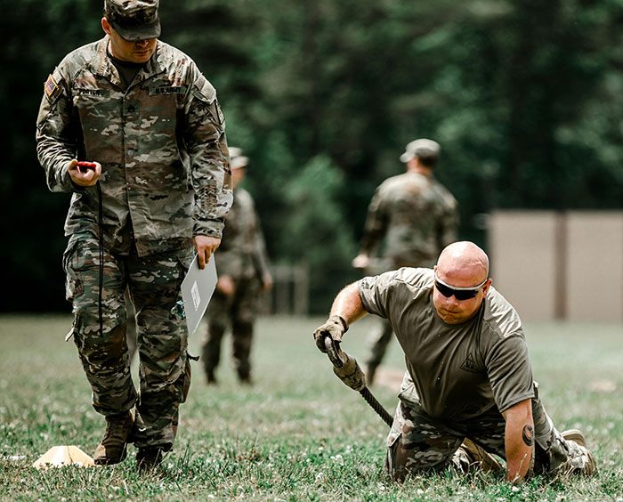 Soldiers training outdoors with one crawling on grass while another times him, showcasing teamwork and discipline today I learned.