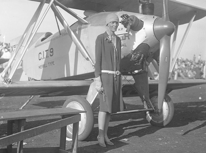 Woman in 1920s outfit standing by vintage airplane, symbolizing cool things people discovered today and new posts.