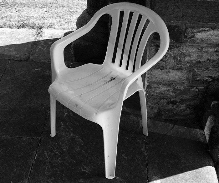 White plastic chair outdoors on stone floor near rustic wall, symbolizing cool things people just discovered.
