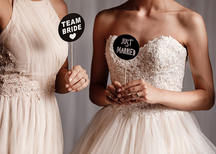 "Bridesmaid and bride in elegant dresses holding 'Team Bride' and 'Just Married' signs, focusing on wedding celebration.