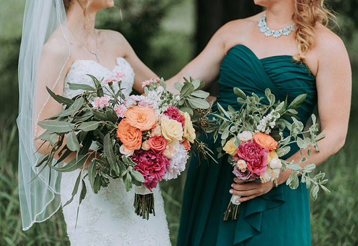 Bride and MOH in elegant dresses holding vibrant flower bouquets, wedding setting.