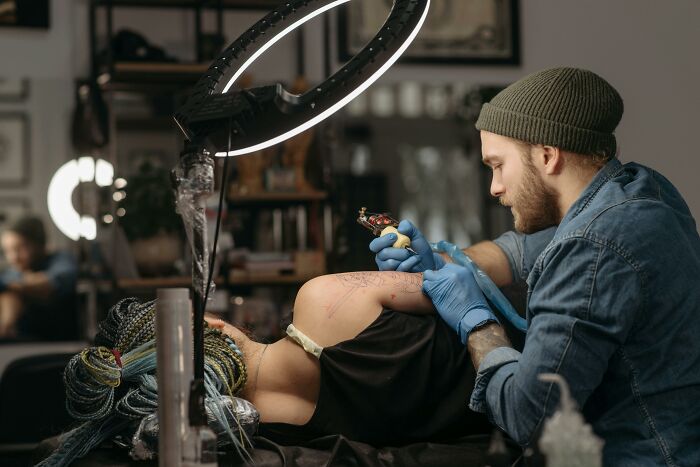Tattoo artist working on a detailed design under bright lighting in a studio.