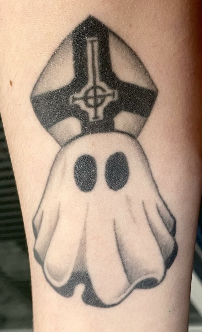 Uncomfortable ghost tattoo with bishop hat and cross detail on skin.