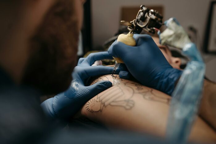 Tattoo artist inking a detailed design on a client's arm, wearing blue gloves for precision and safety.