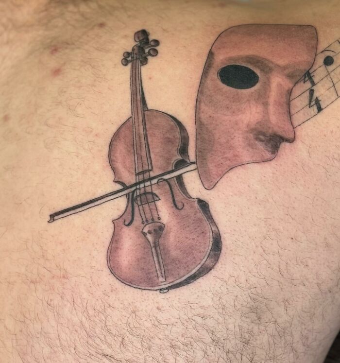 Tattoo of a violin and theater mask, an example of uncomfortable tattoos artists have created.