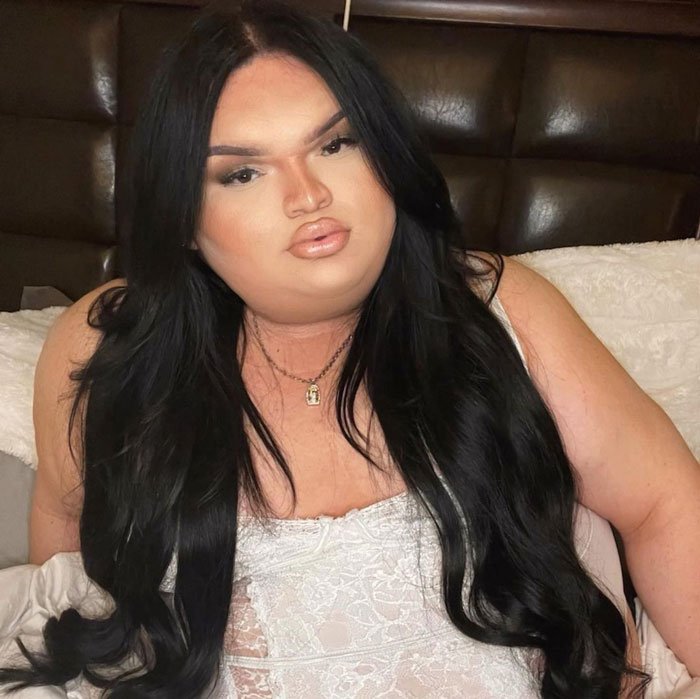 Gorlock The Destroyer, the viral TikTok trans queen, with long black hair, lounging in a white lace outfit.