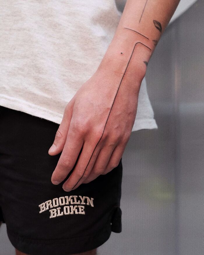 Arm with minimalist tattoos, wearing shorts, featuring unique line designs that artists found uncomfortable to create.