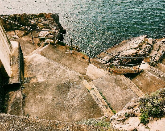 Worn concrete stairs leading down to rocky coastline and ocean, evoking frightening vacation stories by travelers.