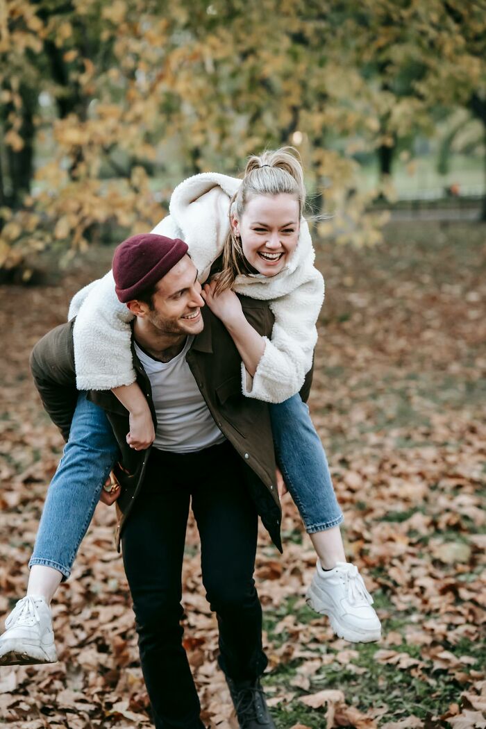 A couple laughing during a piggyback ride in a park, embodying dad humor and joy.