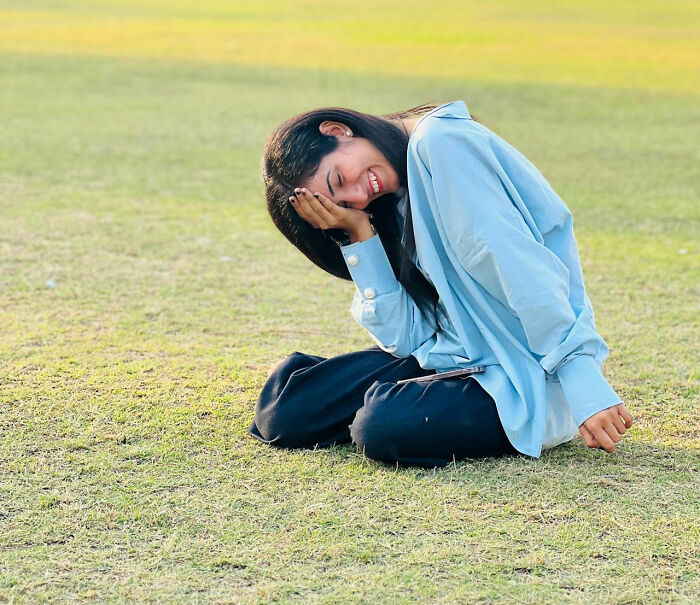 Young woman sitting on grass, laughing with head in hand, embodying dad humor joy.