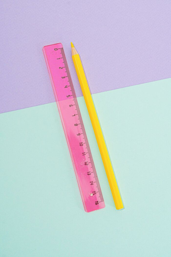 Yellow pencil and pink ruler on pastel background, representing dad humor with simple objects.
